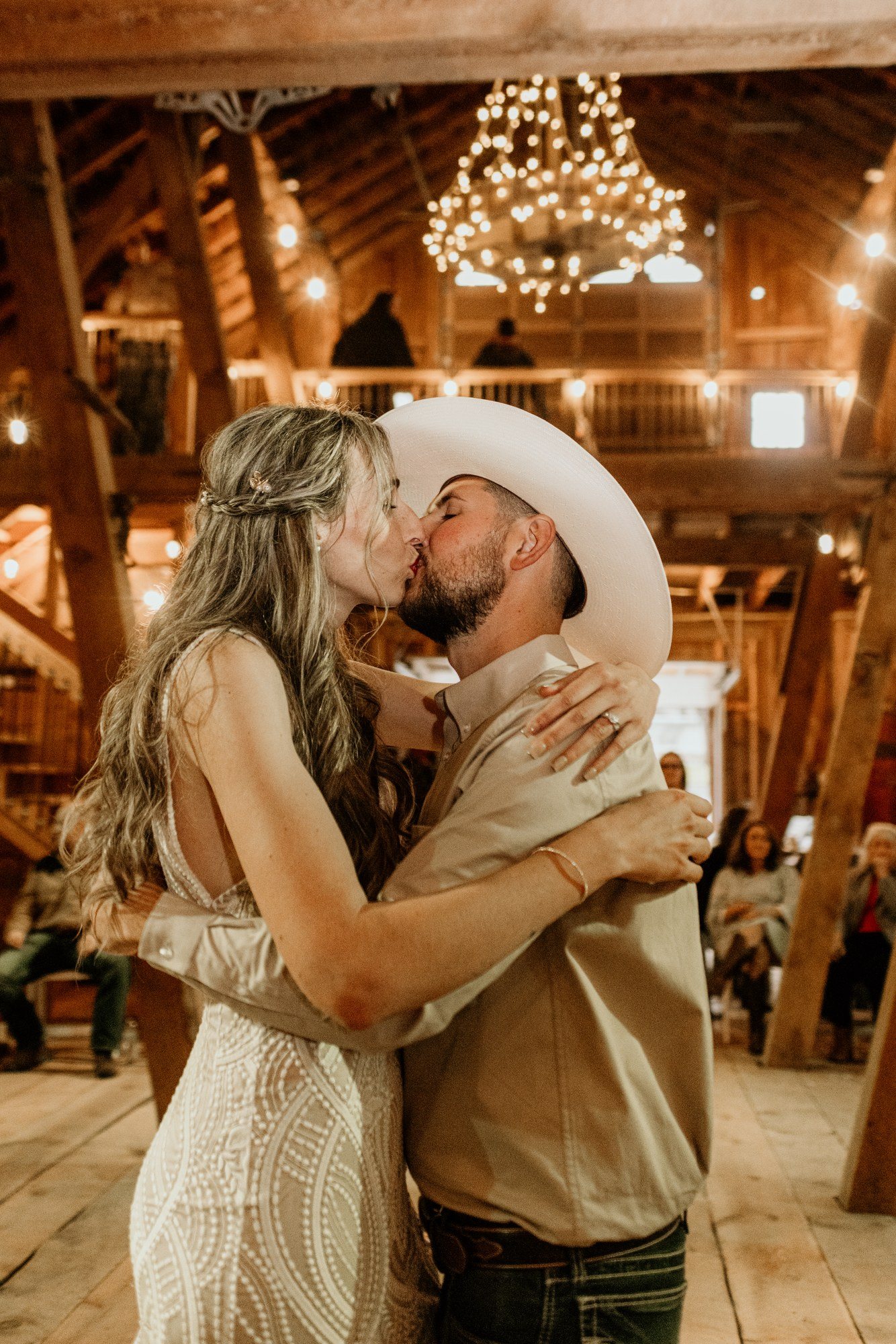 Newlyweds kissing under a chandelier at their barn reception