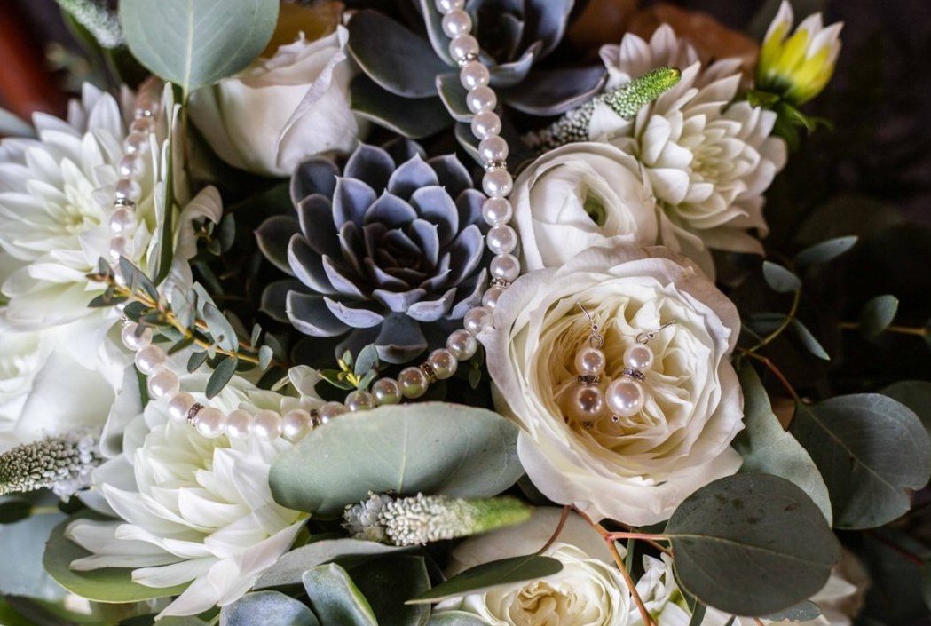 Pearl necklace and earrings resting in a bouquet of roses and succulents