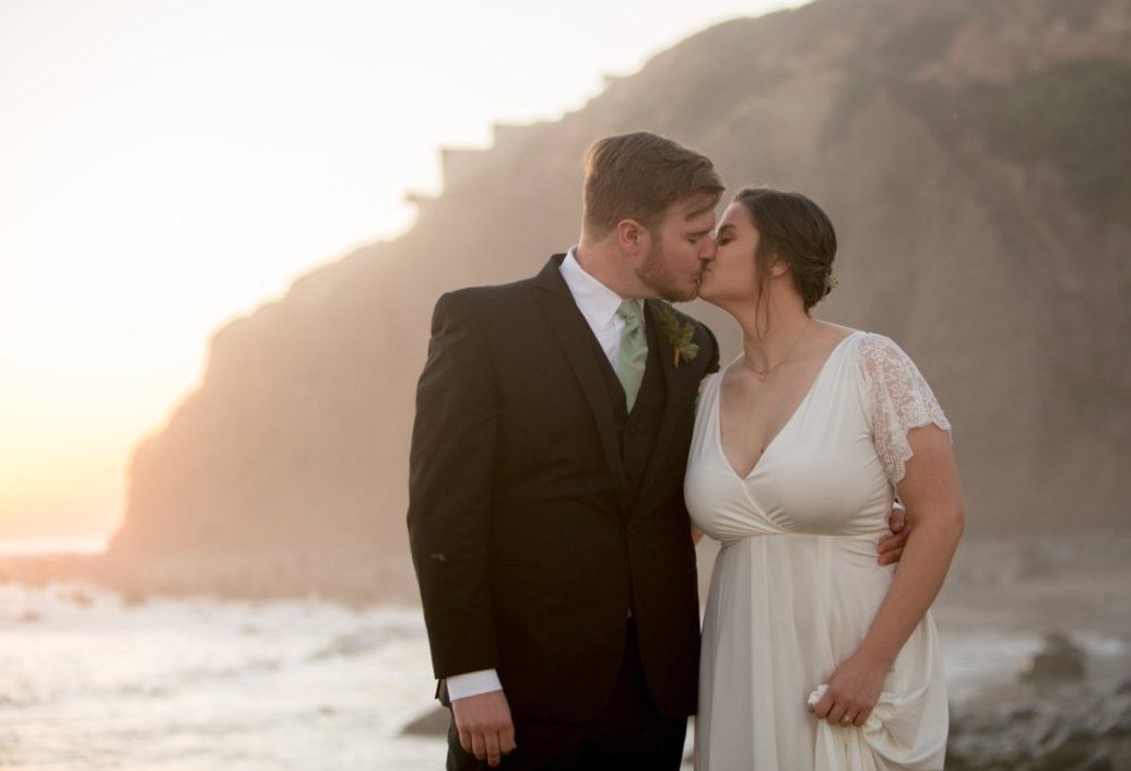 Couple kissing on the beach below a sunlit coastal bluff