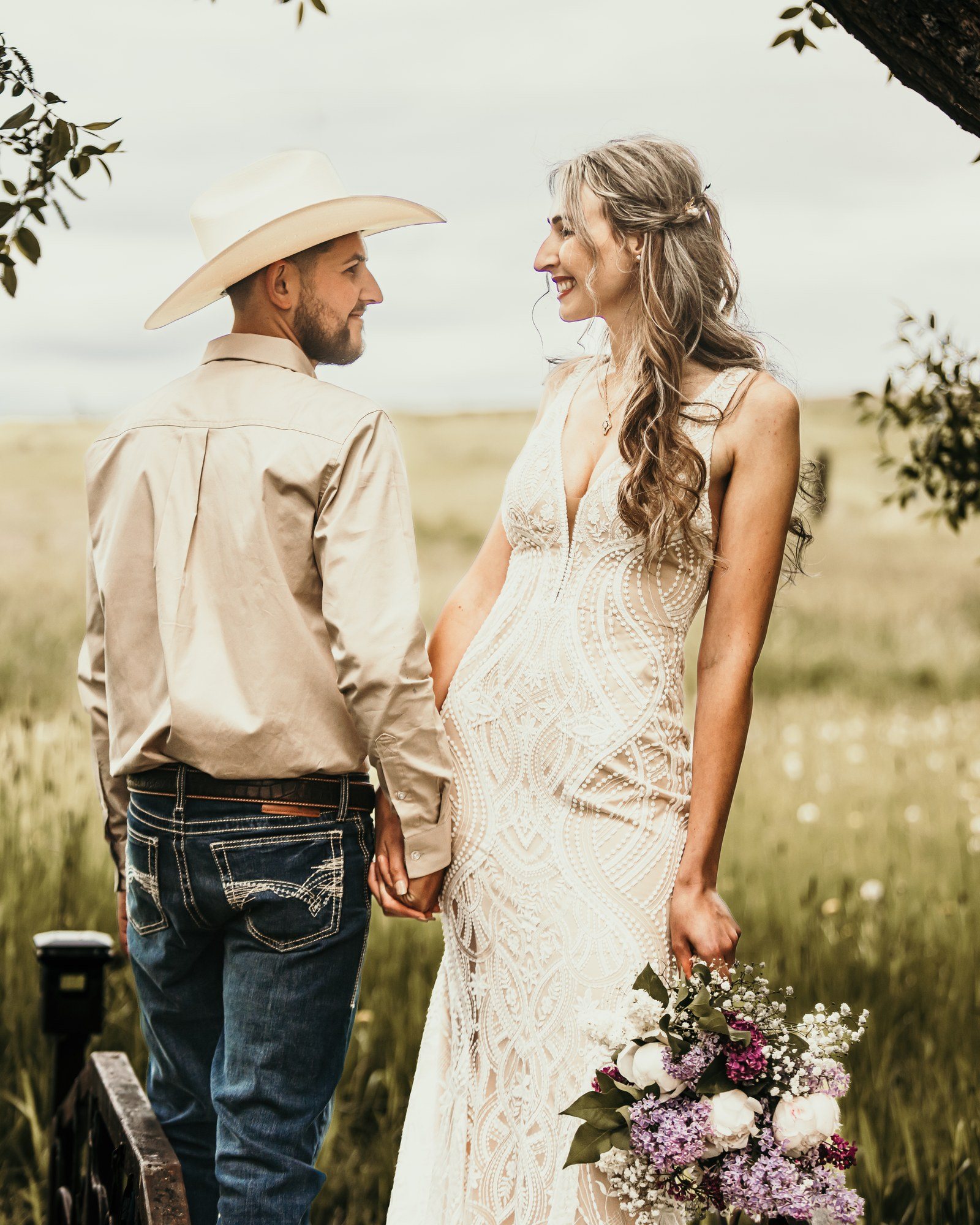 Groom in a cowboy hat holding his bride's hand in a golden field