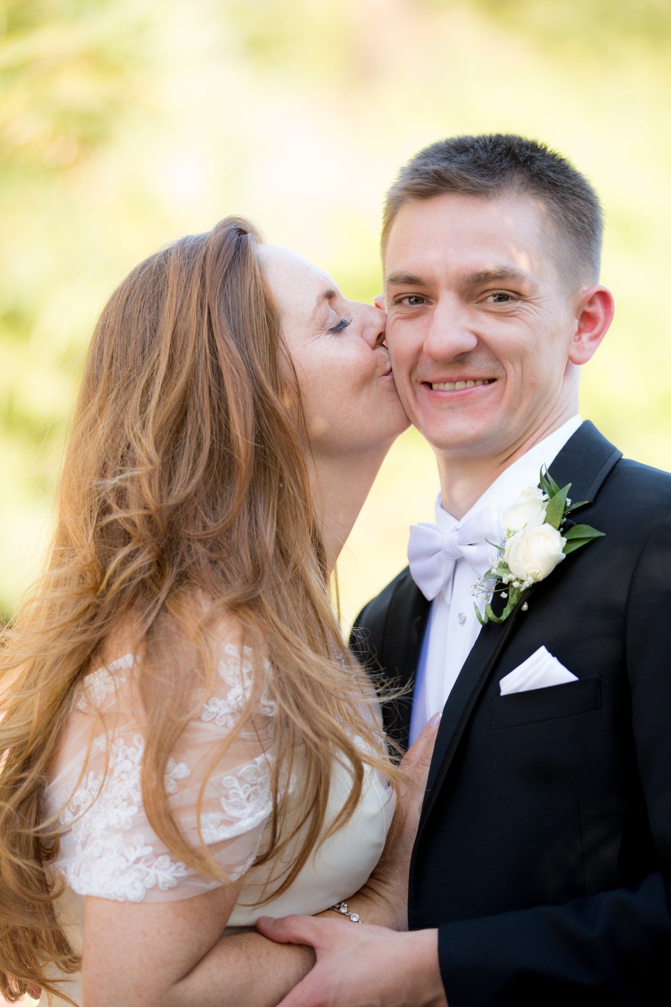 Bride kissing her laughing groom on the cheek in a coastal garden