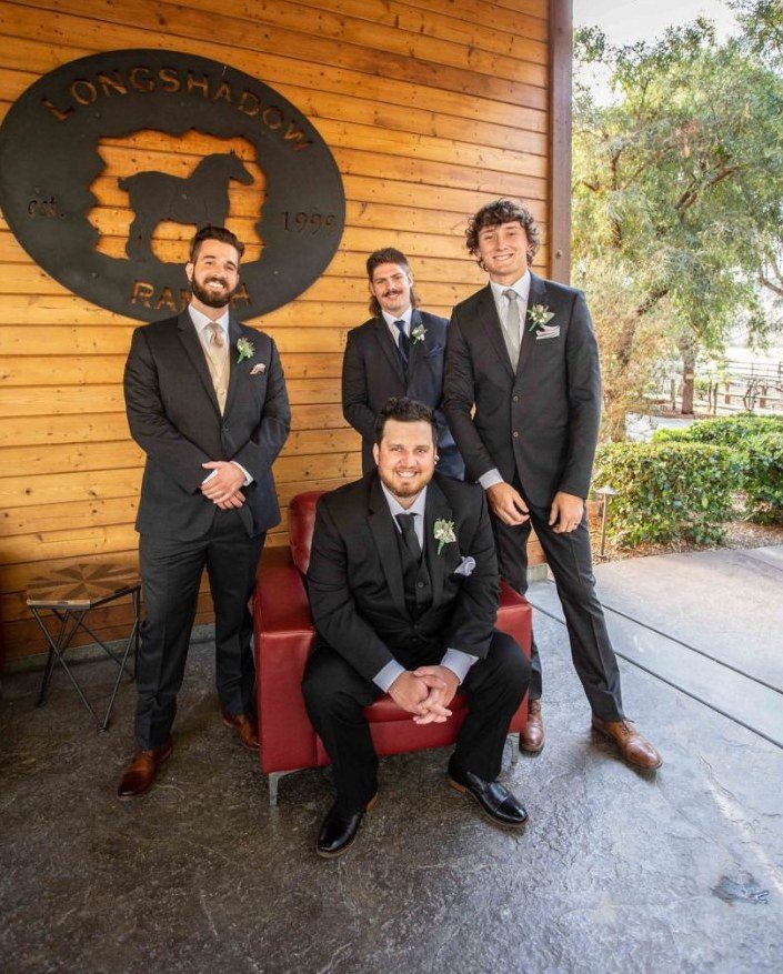 Groomsmen laughing around a red leather chair