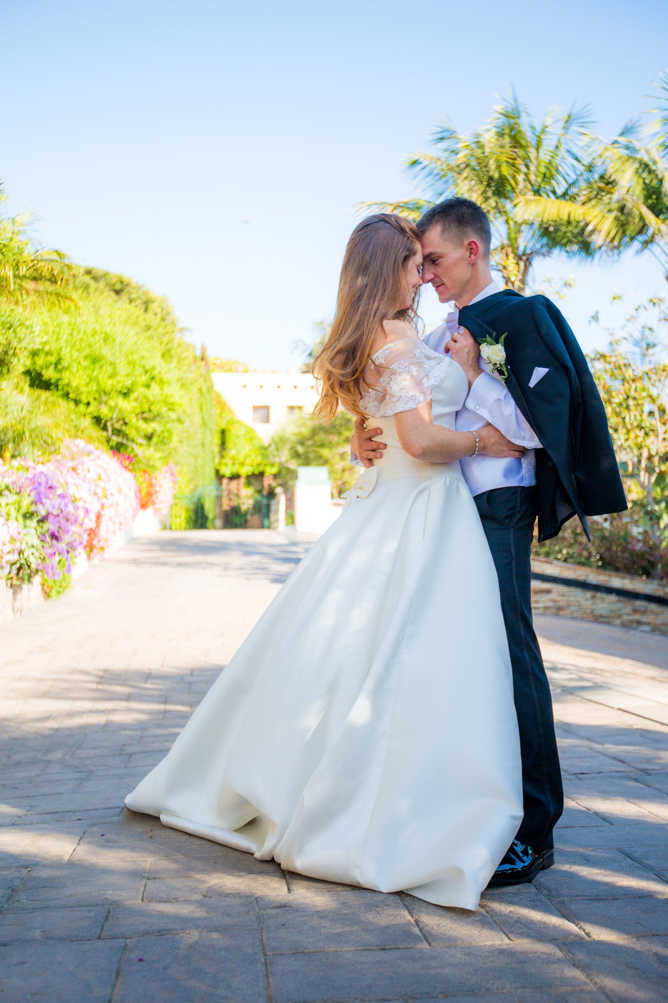 Bride and groom embracing on a garden path above the coast
