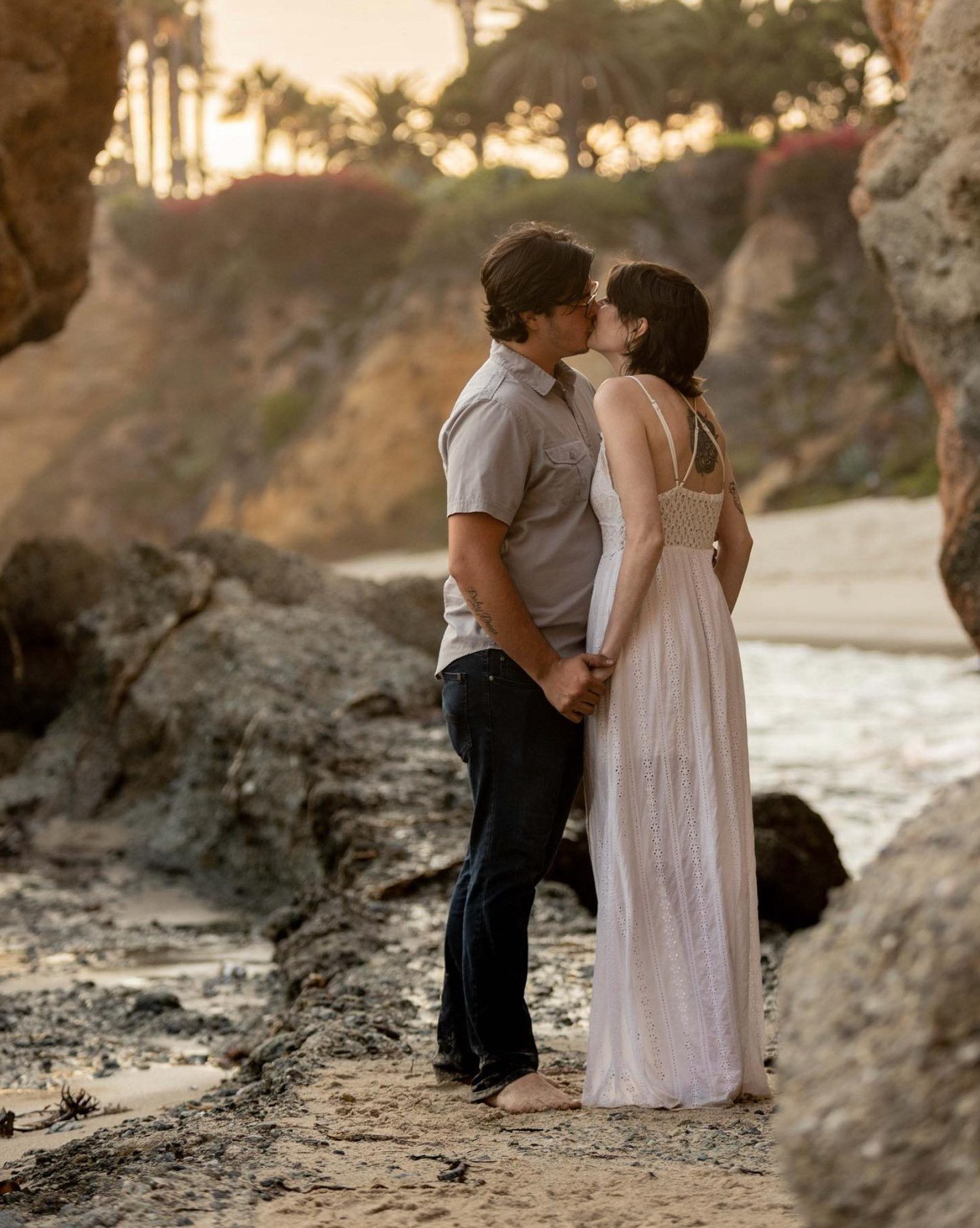Couple kissing barefoot in a rocky beach cove at golden hour