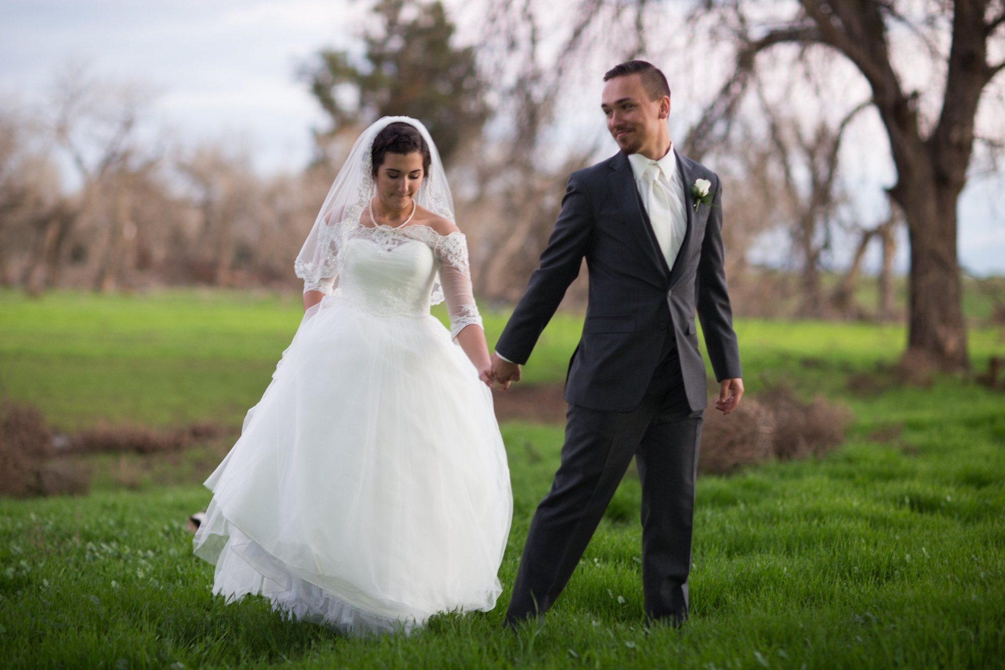 Bride and groom walking hand in hand across a green meadow