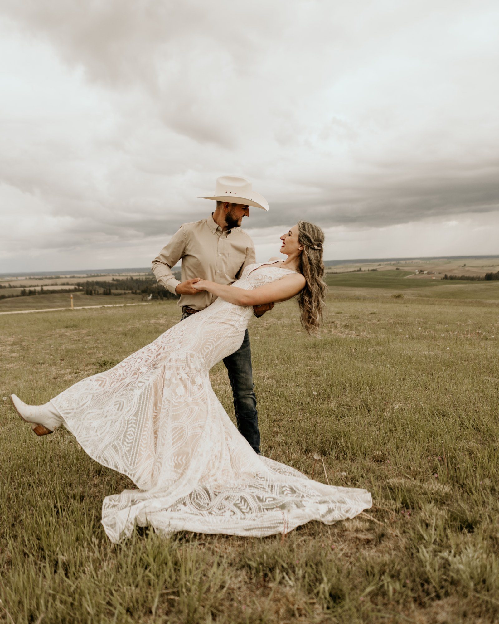 Groom dipping his bride in a mountain meadow under a stormy sky