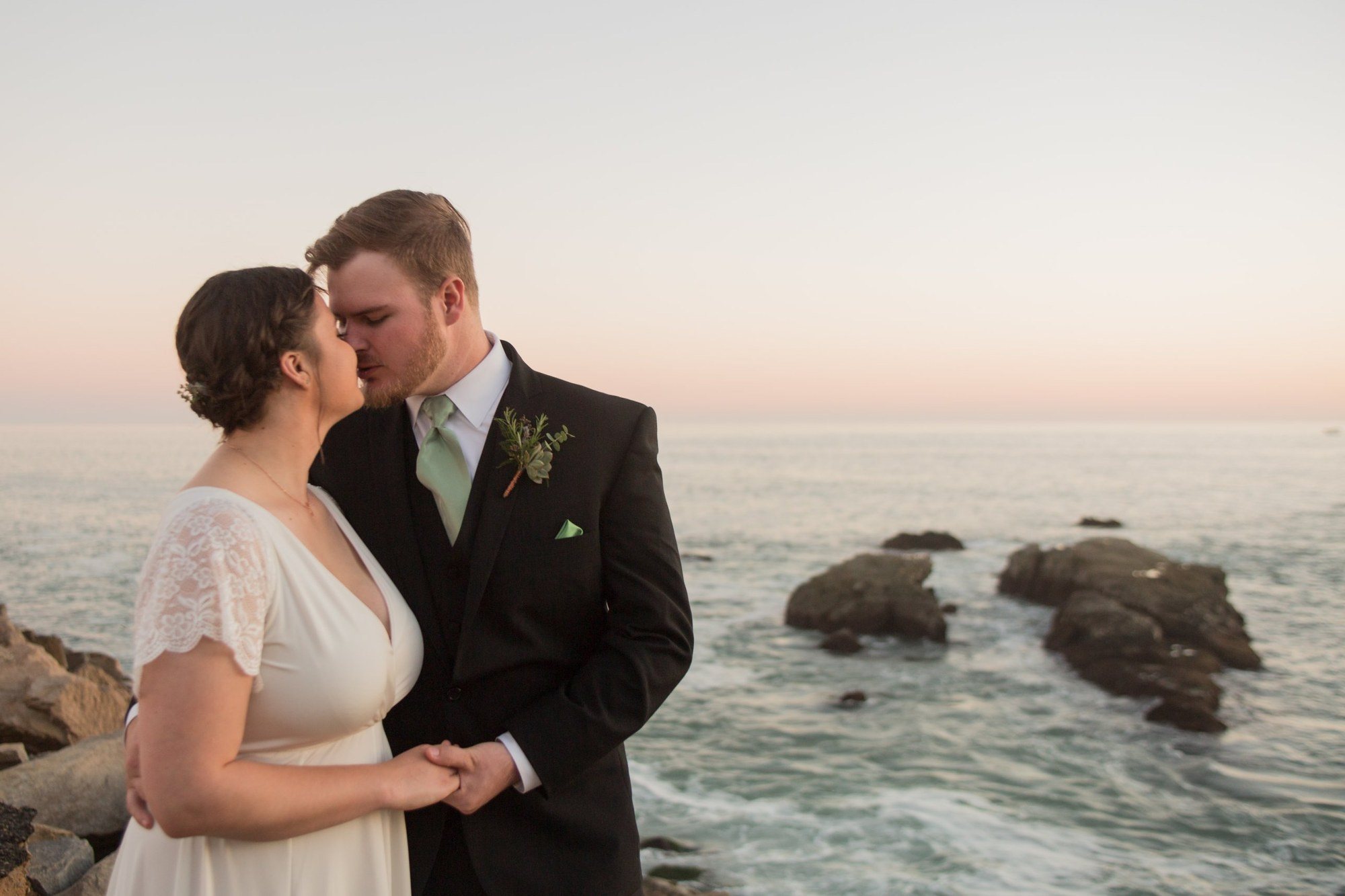 Couple kissing on the rocks above the Pacific at sunset
