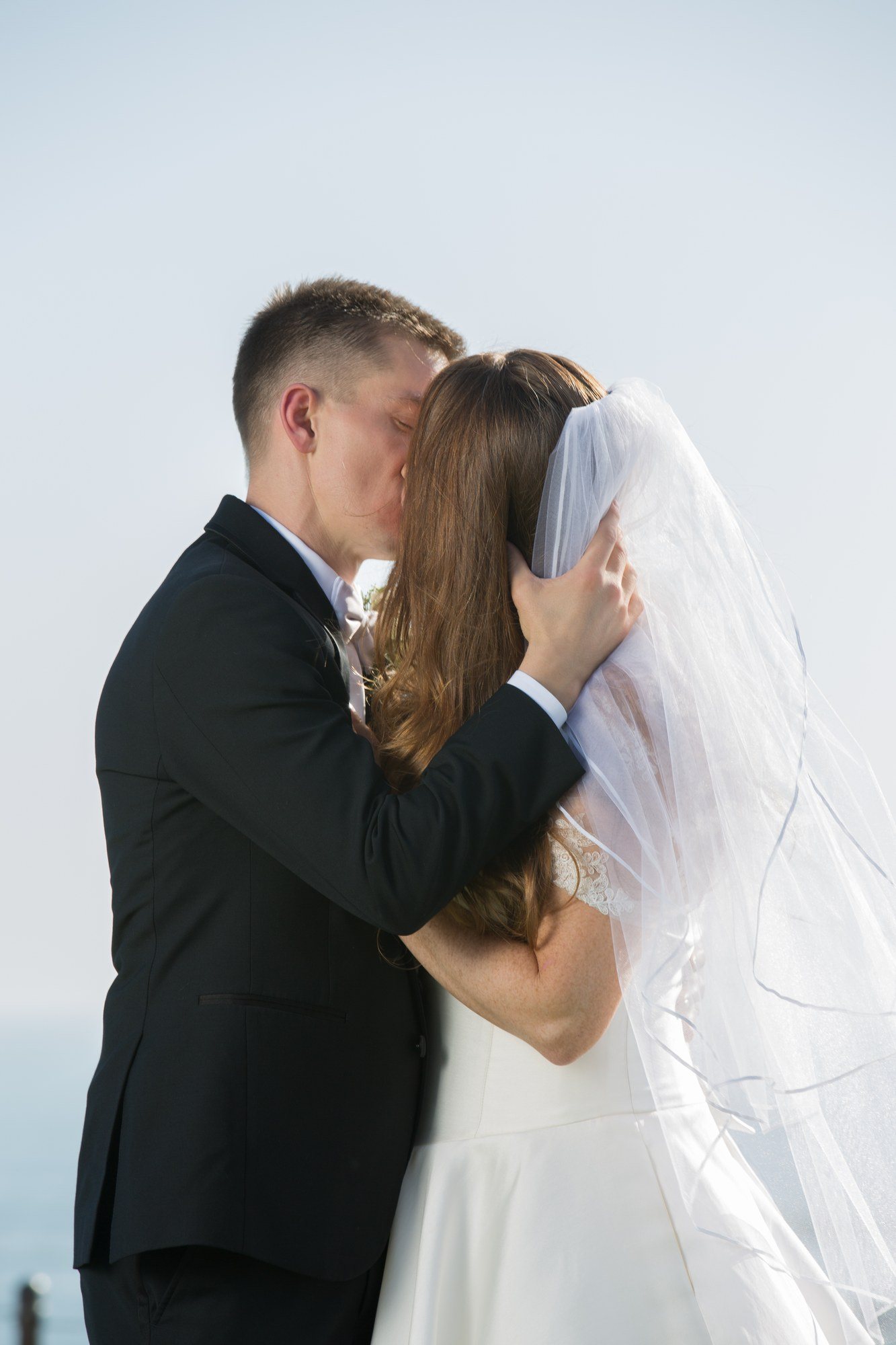 Groom kissing his bride through her veil with the ocean behind