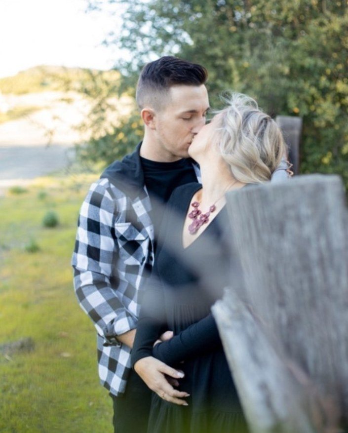 Couple kissing beside a weathered wooden fence