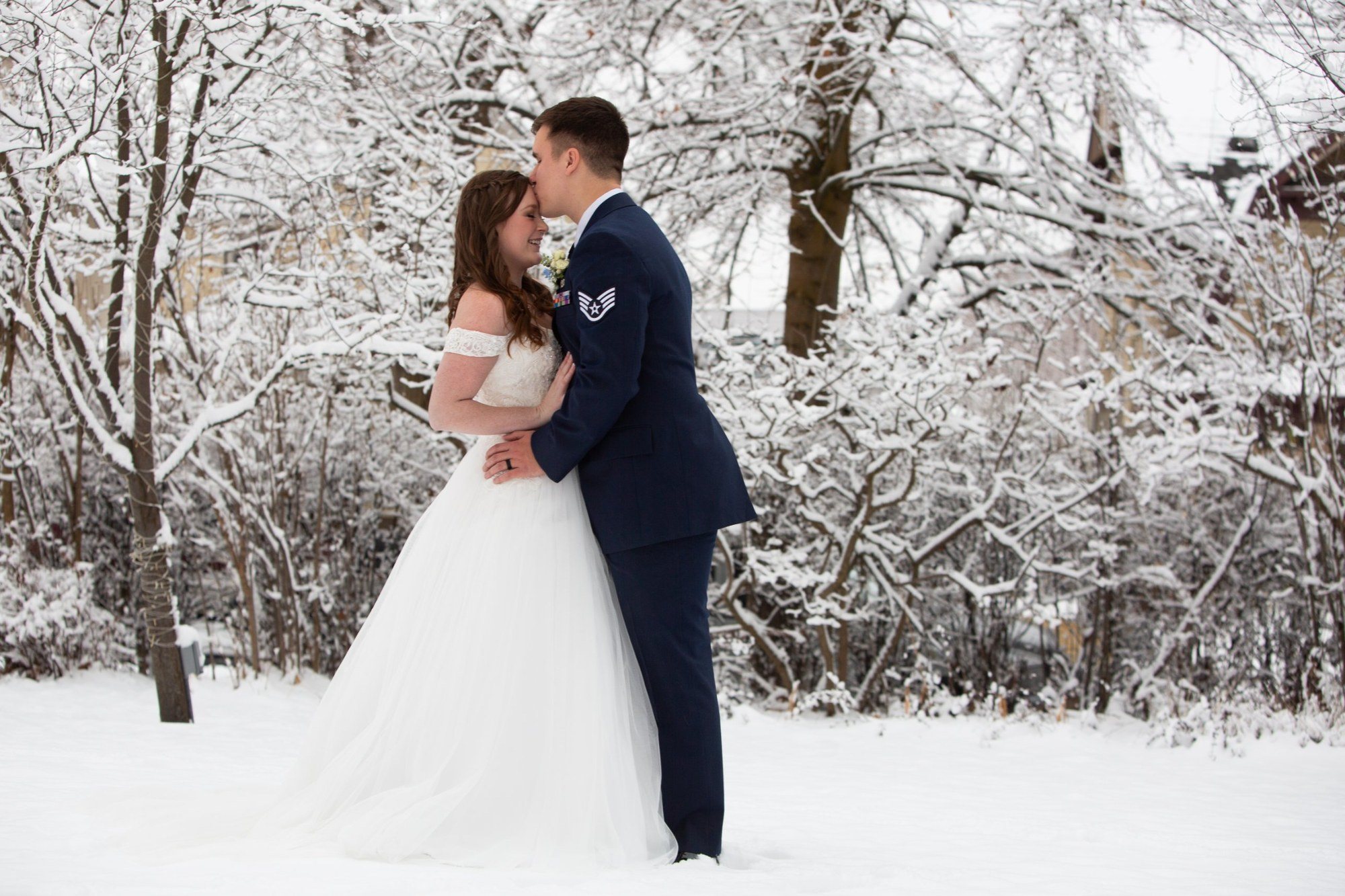 Groom kissing his bride's forehead in a snowy winter garden