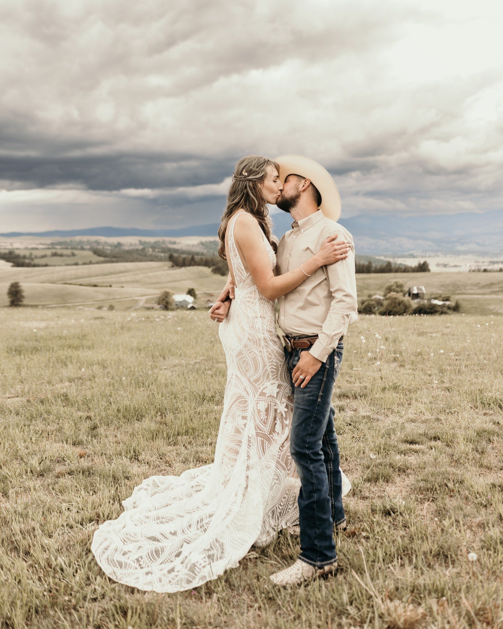 Bride and groom kissing in rolling hills under storm clouds