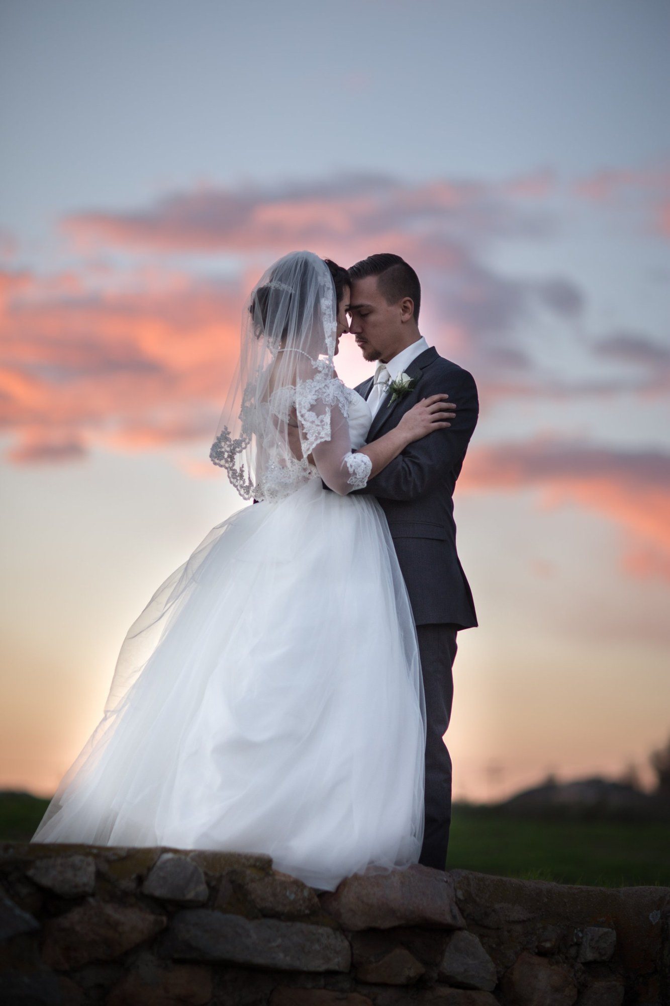 Bride and groom forehead to forehead against a pink sunset sky